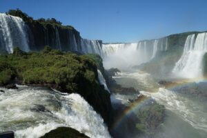 Waterfalls in a rainforest with a rainbow on a clear blue-sky day.
