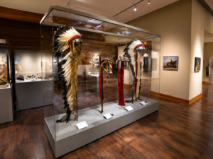 Museum exhibit showcasing Native American ceremonial regalia and cultural artifacts displayed inside a glass case.