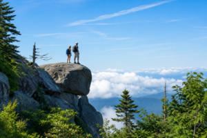 Hikers standing on a rocky mountain overlook above the clouds in Great Smoky Mountains National Park with panoramic views of the surrounding peaks.