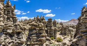 Rugged rock formations and hoodoos rising across a mountain landscape beneath a bright blue sky.