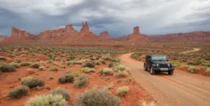 Valley of the Gods Utah: Camping, Hiking & Scenic Drive Guide 6 Jeep traveling along a winding dirt road through the red-rock desert landscape of Valley of the Gods, Utah.