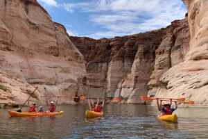 Several people in three canoes wearing life vests, paddling with rocky cliffs in the background.