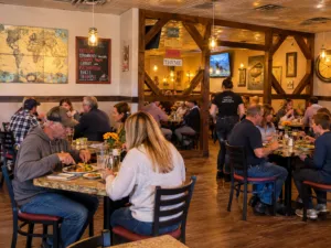 Diners enjoying meals inside a warm, rustic restaurant with wooden beams and casual dining tables.