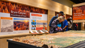 Bryce Canyon Utah Vacation 8 Visitors exploring a Bryce Canyon museum exhibit featuring a detailed landscape model, geology displays, wildlife information, and colorful photographs of Utah’s hoodoos.