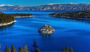 A lake with an island in the middle with mountains ion the background during the winter.