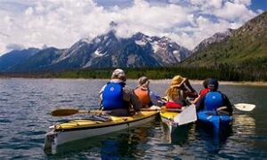 People canoeing on a lake with mountains at a distance with cloud cover.