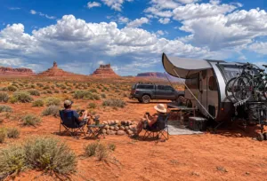 Valley of the Gods Utah: Camping, Hiking & Scenic Drive Guide 4 Couple relaxing beside a travel trailer at a dispersed desert campsite surrounded by the red-rock buttes of Valley of the Gods, Utah.