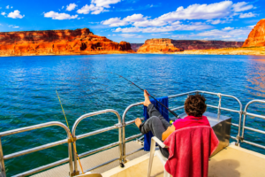 Scenic Lake Powell fishing adventure featuring relaxing pontoon boat views, calm blue water, fishing rods, dramatic red rock canyon cliffs, and peaceful Southwest lake scenery beneath a colorful sky.