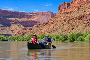 Valley of the Gods Utah: Camping, Hiking & Scenic Drive Guide 5 Two people canoeing along a calm river surrounded by towering red-rock canyon walls and green vegetation in Utah.