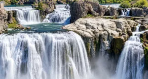 Powerful multi-tiered waterfall cascading over rugged rock formations into blue-green pools surrounded by natural vegetation