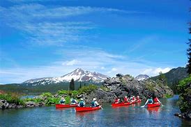 Breathtaking Oregon: How to Vacation in the Cascade Range 3 Several canoes in the water with people wearing life jackets in a forest with mountains and a partly cloudy sky.