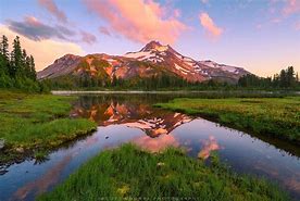 Breathtaking Oregon: How to Vacation in the Cascade Range 4 Lake with vegetation and trees and a tall mountain with a partly cloudy sky.