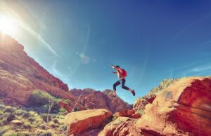 Person leaping from a boulder with ledges and a blue sky