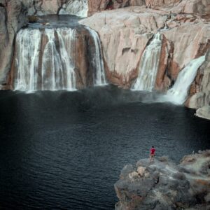 Shoshone Falls Idaho Vacation 4 Person standing on a ledge at waterfalls and a body of water.