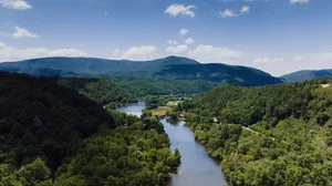 Aerial view of Cherokee National Forest featuring a winding river flowing through lush green woodlands, forested Appalachian Mountains, scenic bridges, and a beautiful blue sky.