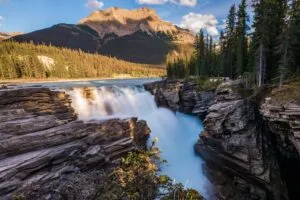 Sunwapta Falls Canada Vacation 2 Sunwapta Falls in Jasper National Park, Alberta, Canada, cascading through a rocky gorge surrounded by evergreen forest and towering Canadian Rockies mountains.