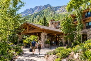 Bridal Veil Falls Utah: Hiking, Waterfalls & Outdoor Adventures 6 Two travelers walking toward a rustic mountain resort entrance surrounded by lush summer greenery and dramatic Utah mountain scenery.