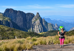 Hiker with a backpack exploring a mountain trail surrounded by dramatic granite peaks, grassy highlands, and expansive scenic views.