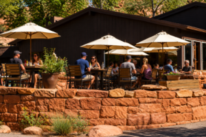 Zion National Park Utah Vacation 8 Visitors enjoying food and drinks at an outdoor restaurant patio surrounded by red sandstone walls and trees near Zion National Park.