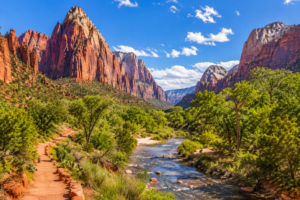 Zion National Park Utah Vacation 1 Panoramic view of Zion National Park featuring towering red sandstone cliffs, lush green trees, the Virgin River, and a scenic hiking trail beneath a bright blue sky.