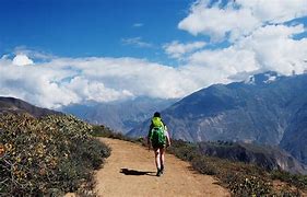 Explore Colca Canyon, Peru: Ultimate Adventure & Vacation Guide 3 Person with backpack walking on a trail at a canyon with mountains and a partly cloudy sky.