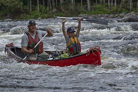 People canoeing in a river wearing life vests in a forest