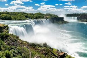 large waterfalls with steep cliffs and trees with a partly cloudy sky.