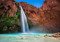 waterfalls with steep cliffs and people laying out in the sun on a clear blue-sky day