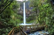 waterfalls with steep cliffs and a wooden bridge with a river flowing and trees