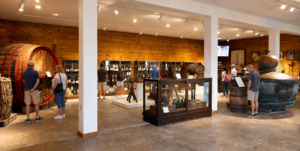 Explore New York’s Scenic Finger Lakes Region 6 Visitors exploring a museum gallery with historic barrels, bottles, equipment, artifacts, and informational displays.
