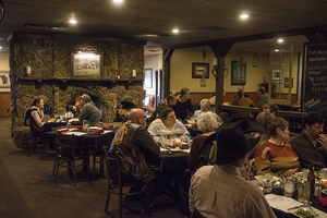 Guests enjoying dinner at a rustic Wyoming steakhouse near Bighorn National Forest, featuring a large stone fireplace, wooden furnishings, and a welcoming Western atmosphere.
