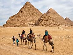 People riding on camels at the pyramid of Egypt on a cloudy day.