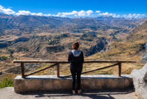 Explore Colca Canyon, Peru: Ultimate Adventure & Vacation Guide 5 Visitor enjoying a breathtaking panoramic view from a scenic overlook above Colca Canyon, Peru, surrounded by rugged Andean mountains.