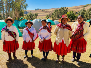 Explore Colca Canyon, Peru: Ultimate Adventure & Vacation Guide 6 Group of Indigenous Andean women wearing traditional clothing in the Colca Canyon region of Peru with the Andes and campsites in the background.