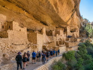 Visitors walk through the spectacular ancient cliff dwellings of Mesa Verde National Park, Colorado, exploring remarkably preserved Ancestral Pueblo stone villages built beneath a towering sandstone alcove.
