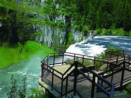 waterfall with steel walkway and steep cliffs and forest and water at the bottom.