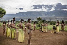 Angel Falls Venezuela Vacation 2 People doing a ceremonial dance in a rainforest with large mountains in the background.