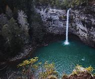 Waterfall with steep cliffs emptying into a large pool of water in a forest.