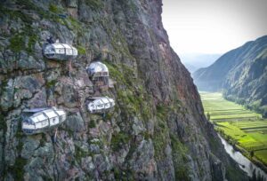 Four cliffside glamping units built directly into steep canyon walls overlooking the Sacred Valley near Cusco, Peru, with dramatic mountain views and the valley far below.