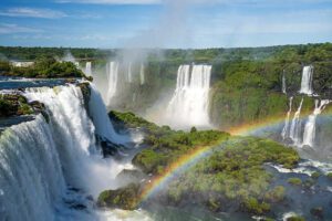 Iguazu Falls Photography Tours 1 Iguazu Falls cascading through lush rainforest with a rainbow arching over the waterfalls — a breathtaking natural wonder. 🌈🐒🌿