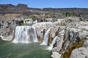 Shoshone Falls near Twin Falls, Idaho, with powerful waterfalls cascading over rocky cliffs into the Snake River beneath a clear blue sky.