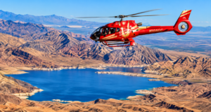 Red sightseeing helicopter flying above a brilliant blue lake surrounded by rugged desert mountains and expansive canyon landscapes.