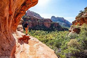 hiker with backpack on ledge looking at a forest and steep cliff canyon during the day.