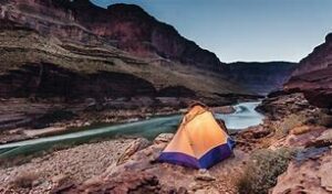Sedona Canyon Hiking And Vacation Tours 3 camping tent next to river in a canyon with steep cliffs near nighttime