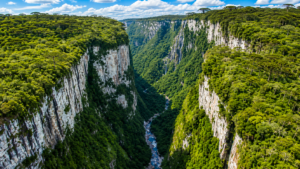 Aerial view of Itaimbezinho Canyon in southern Brazil, featuring towering rocky cliffs, dense green forest, waterfalls, and a winding river deep within the canyon.