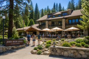 Kings Canyon, California, Camping And Hiking 6 Exterior of John Muir Lodge at Kings Canyon National Park with visitors relaxing on the outdoor patio and hikers walking toward the entrance surrounded by towering pine trees.