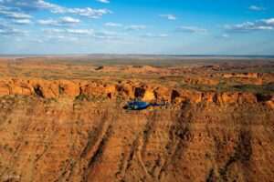 Helicopter flying over a vast canyon with towering canyon walls and a partly cloudy blue sky