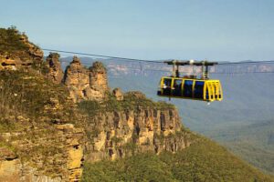 Cable car gliding above a lush forest in a deep valley, surrounded by steep cliff walls, moving across scenic mountainous terrain.