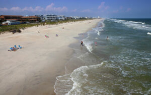 People enjoying a sandy beach next to the ocean with a building visible in the background.