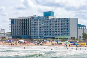 Kure Beach, NC, Camping And Hiking Tours 7 Oceanfront hotel overlooking a busy sandy beach with swimmers, umbrellas, and rolling waves.